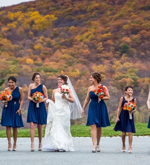 Bride walking with her bridesmaids, wearing short blue dresses, among the fall mountains.