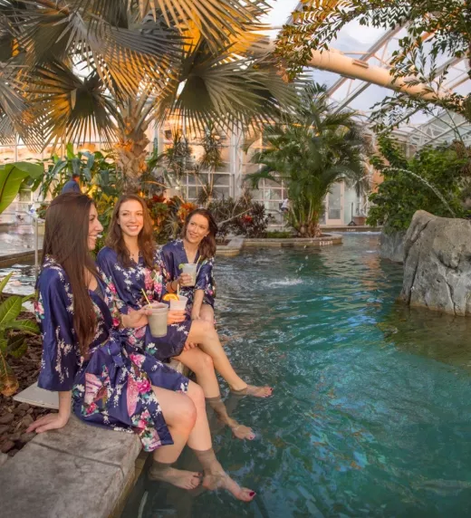 Four women in floral robes sitting on edge of Biosphere pool.
