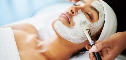 Tech painting white face mask on woman's face during spa treatment.