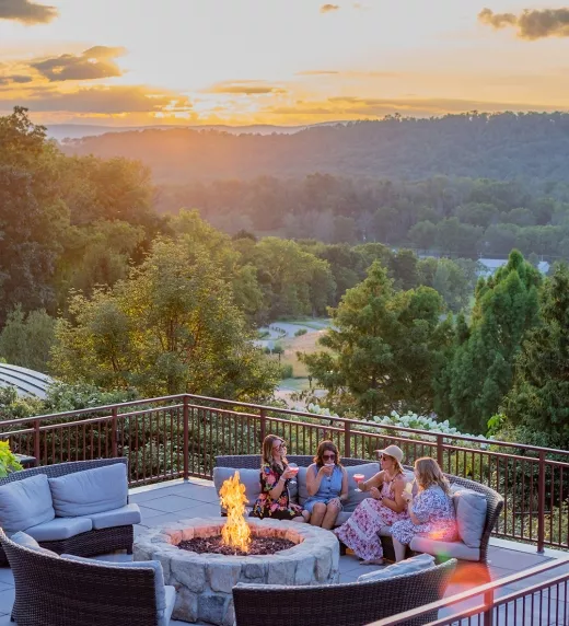 Group of four girlfriends sitting around firepit on Fire & Water terrace overlooking sunset mountain views.