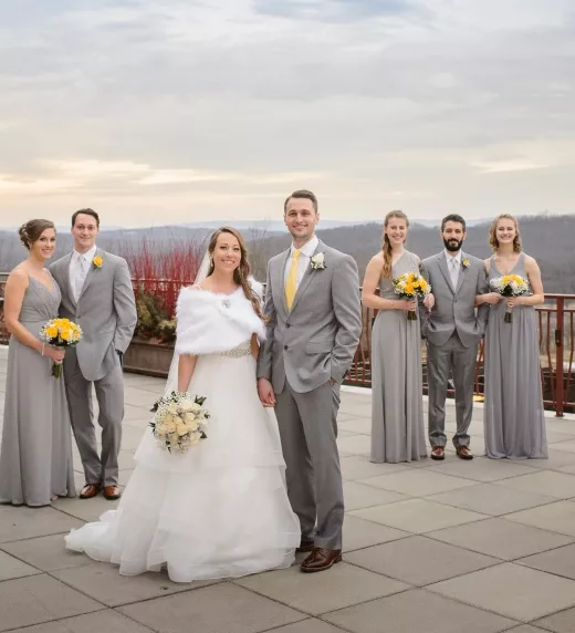 Bridesmaid, groomsmen, and groom wear grey and stand together on the Fire & Water Terrace. 