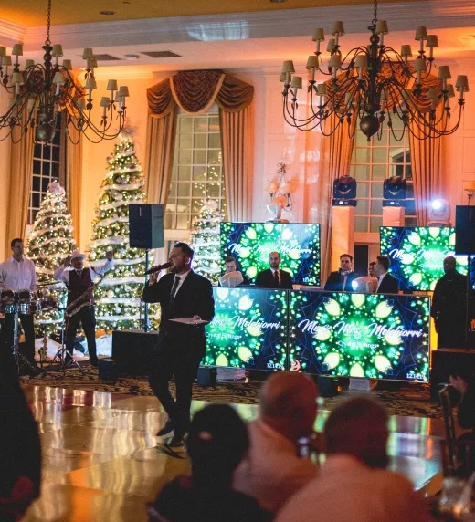 Winter wedding reception featuring man speaking on microphone with 4 large tv screens behind him.