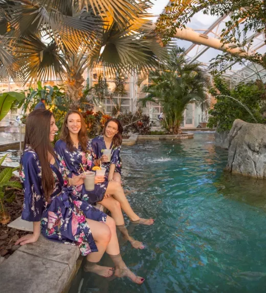 Four women in floral robes sitting on edge of Biosphere pool.