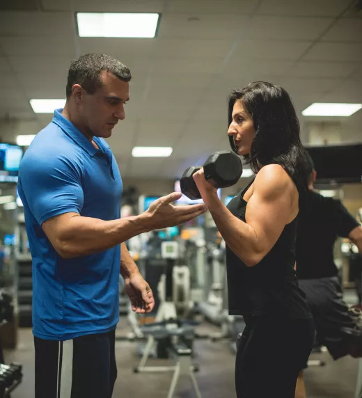 Woman doing bicep curls with personal trainer's assistance.