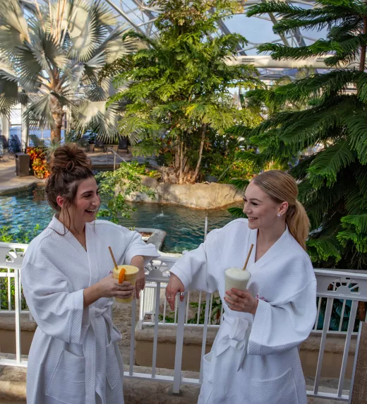 Two women in white robes drinking in Biosphere Pool Complex