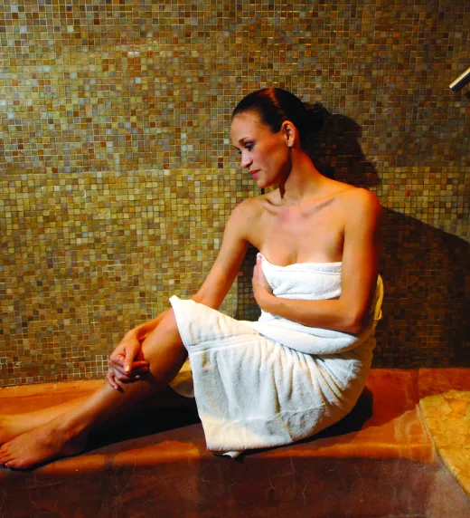 Woman in white towel sitting in sauna.