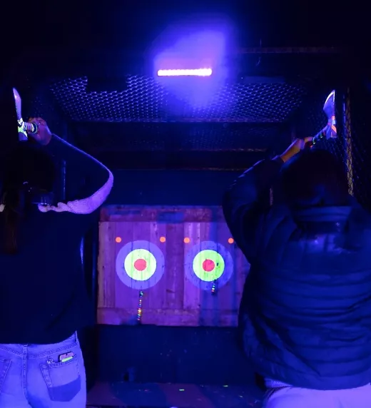 Two people throwing axes during glow in the dark axe throwing.