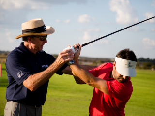 Golf instructor giving lessons to man in red shirt