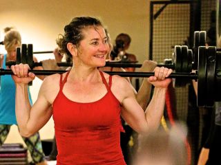 Woman standing in red shirt lifting a weight.