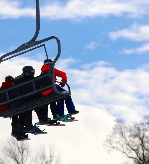 Three people sitting on ski lift.