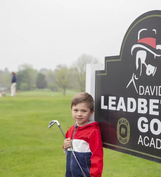 Young boy standing in front of the Leadbetter Golf Academy sign