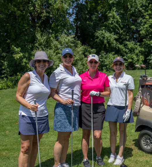 Group of four women standing next to a golf cart