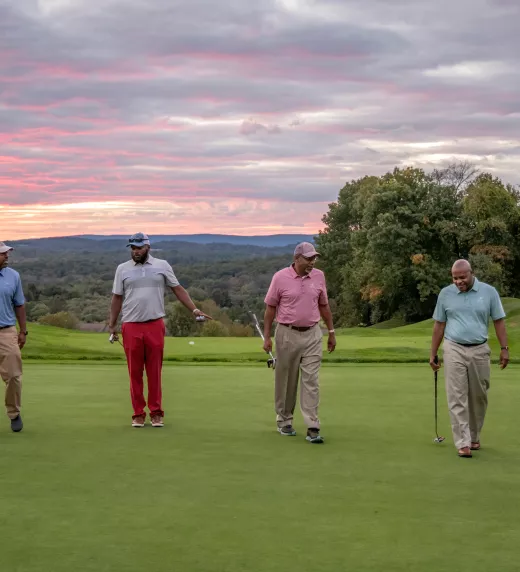 Guys foursome walking on a golf course with the sunset in the background