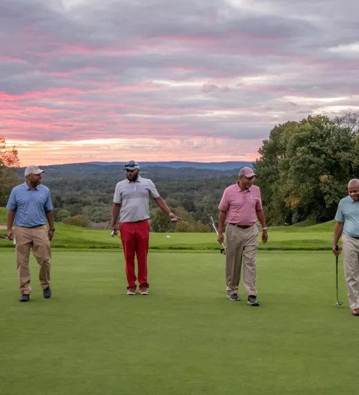 Guys foursome walking on a golf course with the sunset in the background