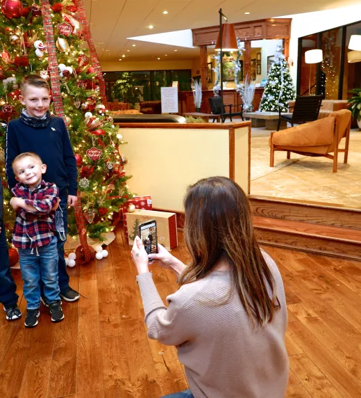 Mom taking photo of three sons in front of Christmas tree