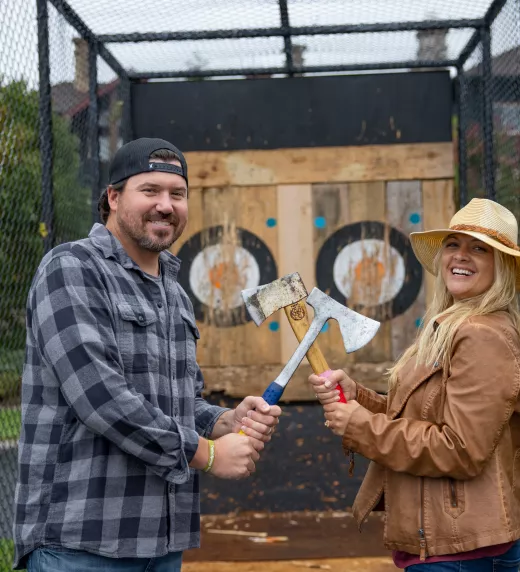 Woman and man holding axes in front of axe throwing target during couples getaway.