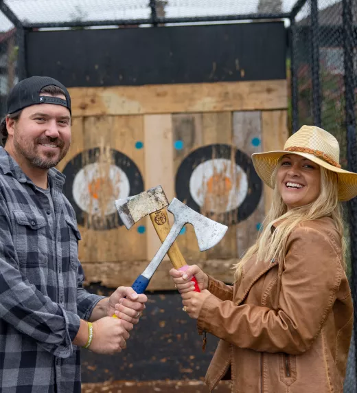 Woman and man holding axes in front of axe throwing target during couples getaway.