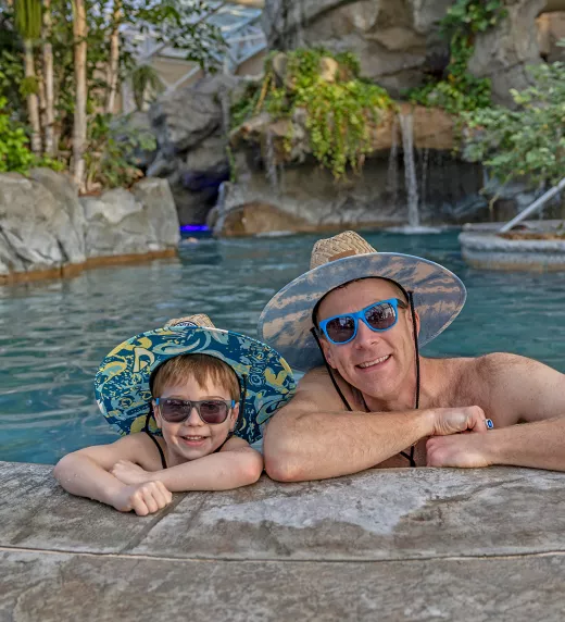 Father and son wearing matching hats and sunglasses in Biosphere pool.